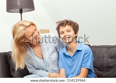 A beautiful woman and her teenage son at home, sitting on a couch laughing.