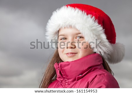 Cute young girl standing outside, wearing a red Santa hat,looking into the camera