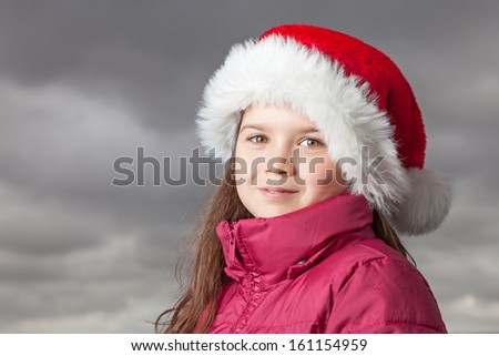 Cute young girl standing outside, wearing a red Santa hat,looking into the camera