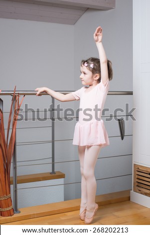 Little girl wearing a ballet dress is practicing ballet in a dance studio