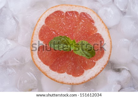 Composition of fresh red grapefruit slices with ice cubes and mint herb leaf.