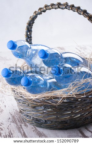 Couple of sparkling water blue bottles in a wooden basket on a bright wood background,