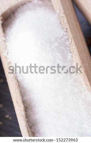 Close up photo of white sugar in a spatula on a dark solid wooden background.