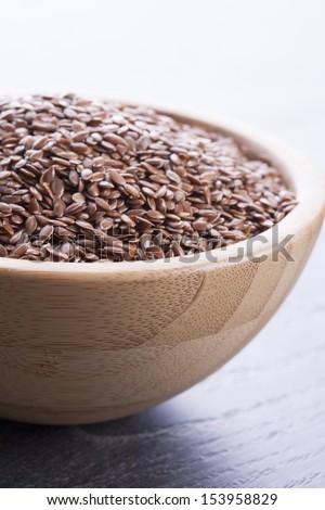 Close up photo of a raw eco food in the wooden bowl - dark brown linseeds placed on a dark wooden background.