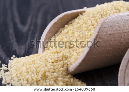 Close up photo of a raw eco food in the wooden spatulas - light yellow couscous placed on a dark wooden background.