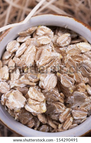 Close up photo of a cereal grain product in a clay cup - dark brown secale flakes placed on a wooden shavings.