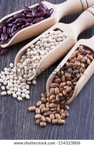 Close up photo of a beans in wooden scoop - brown pinto beans, red beans and white beans placed on a dark wooden background.
