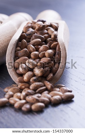 Close up photo of a beans in wooden scoop - brown pinto beans placed on a dark wooden background.