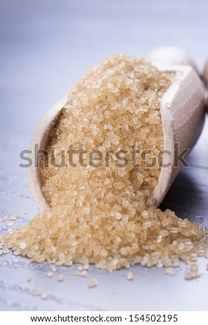 Close up photo of a food ingredients in a wooden scoop - brown sugar cane placed on a dark wooden background.
