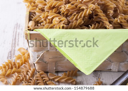 Raw food composition - brown rotini pasta placed on a bright background.