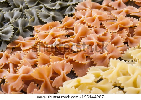 Raw food composition - yellow, orange and green farfalle pasta close up photo.