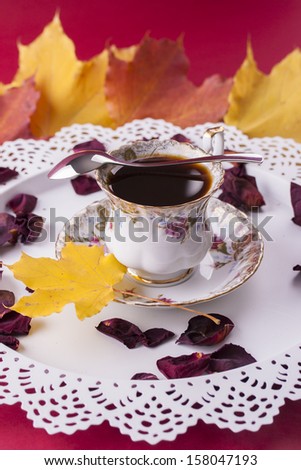 Autumn style close up photo of a hot coffee cup placed at white bright try decorated with some leafs.