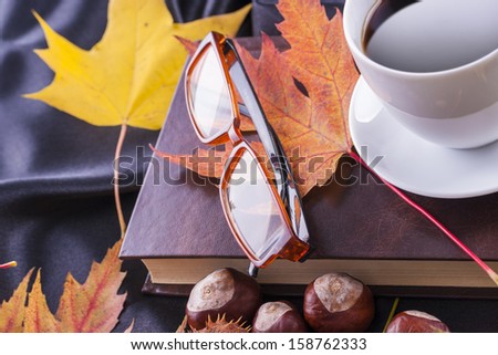 Autumn style close up photo of a hot coffee cup with eyeglasses placed on the top of a book.