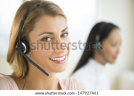 Close-up portrait of happy female customer service representative with colleague in background