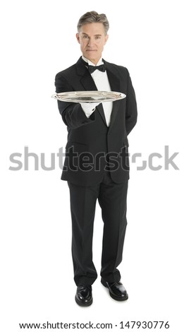 Full length portrait of confident mature waiter with tray standing against white background