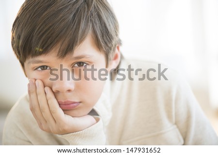 Close-up portrait of bored boy with hand on chin at home