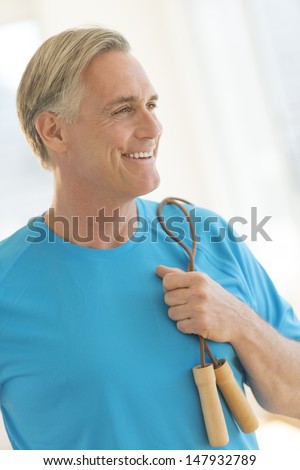 Happy mature man with jump rope looking away in gym