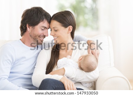 Relaxed young couple with cute little baby sitting on couch