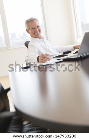 Portrait of happy mature businessman writing on document at desk in office