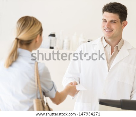 Male pharmacist receiving prescription paper from customer at medical store