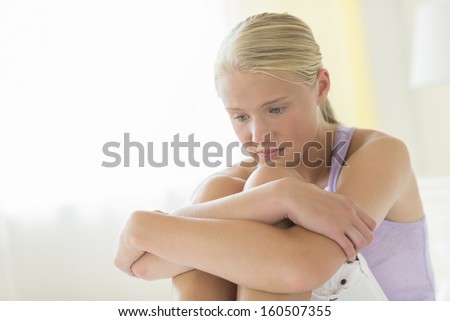 Depressed teenage girl hugging knees while sitting on bed