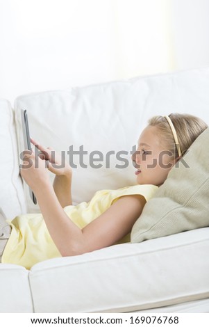 Profile shot of girl using digital tablet while lying on sofa at home