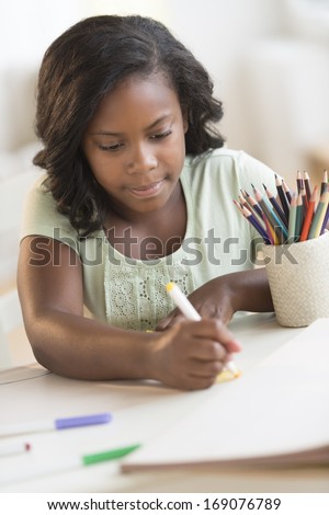 Girl with felt tip pen coloring at table in house
