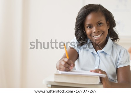 Portrait of girl smiling while writing notes in book at classroom desk