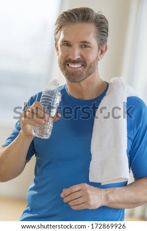 Portrait of mature man drinking water from bottle after exercising at home