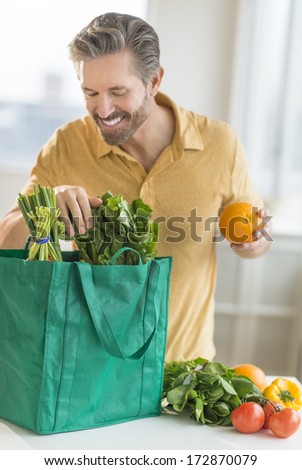 Happy mature man unpacking bag of groceries at counter top