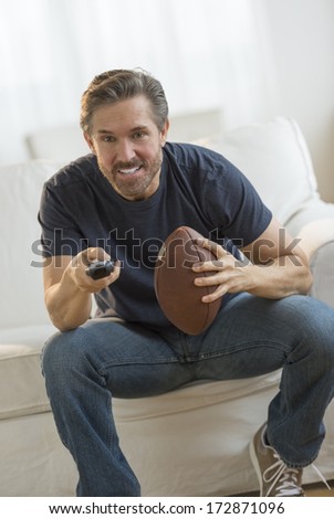 Excited mature man with American football watching TV on sofa