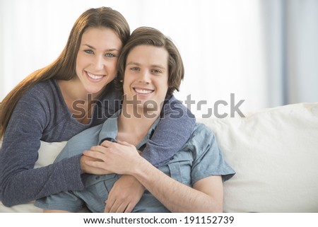 Portrait of loving woman embracing man from behind in living room