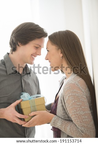 Affectionate young man giving birthday gift to woman at home