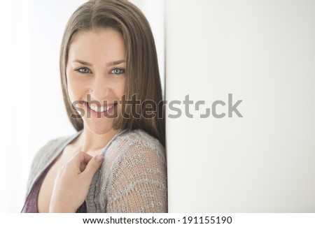 Portrait of beautiful young woman smiling while leaning on wall at home