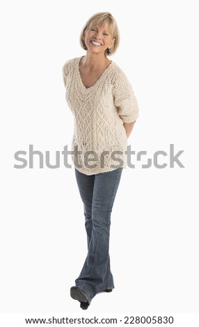 Full length portrait of happy mature woman with hands behind back walking over white background