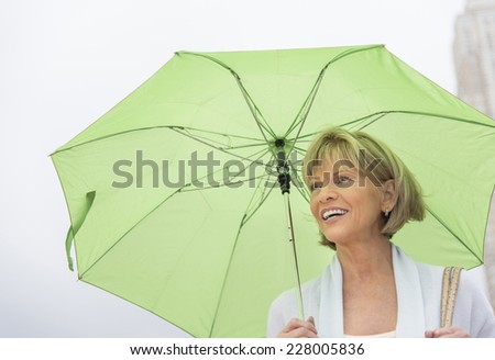 Happy mature woman with green umbrella looking away against clear sky