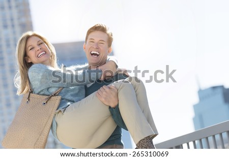 Portrait of mature man laughing while lifting woman in city