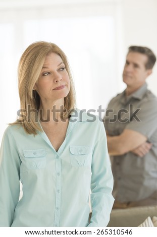 Angry mature woman looking away with man standing in background at home