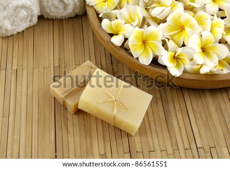 bowl of many frangipani with natural handmade soap and towel on bamboo mat