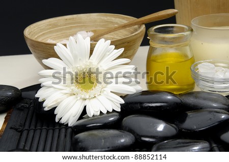 gerbera with massage oil and herbal salt in spoon on bowl and stones
