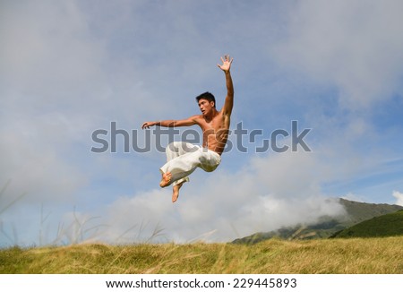 male model with muscles in exercise jumping outdoors. over mountain grass