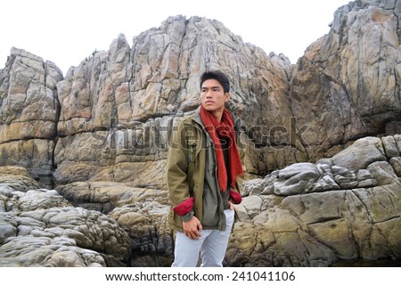 young man in scarf with coat  on a rock at beach