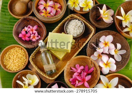 spa setting with massage oil , salt in bowl ,candle, frangipani,spoon