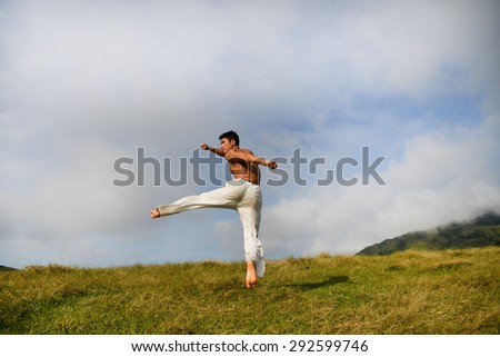 male model with muscles in exercise jumping outdoors. over mountain grass