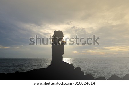 Silhouette of woman praying over beautiful sunset background