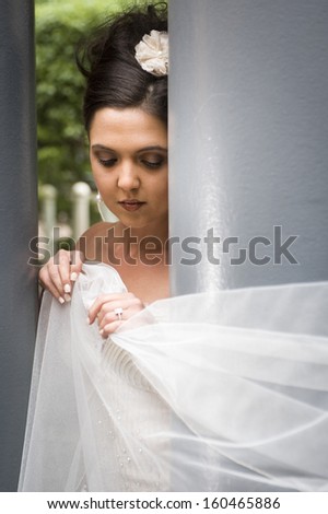 Young beautiful caucasian woman standing between two blue columns holding white veil looking away from camera
