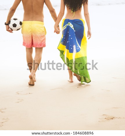 young couple walking along beach with Brazil flag and football