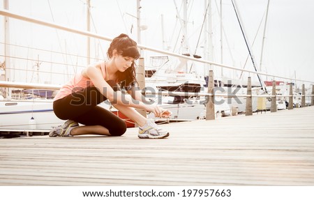 Young athletic runner tying shoe laces on wooden deck