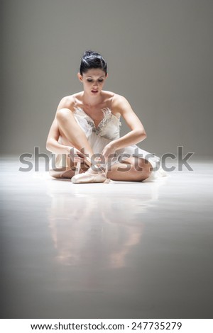 Young beautiful ballerina sitting under spotlight with pointed ballet shoes