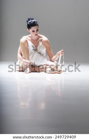 Young beautiful ballerina sitting on floor with ballet shoes